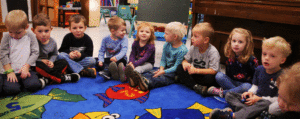 An image of children sitting around a rug in a classroom.