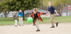 An image of children playing on the playground, with one boy chasing a ball.