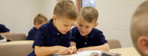 An image of 2 boys reading a book together in the classroom.
