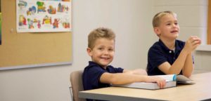 An image of 2 smiling boys sitting in a classroom.