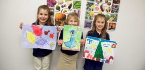 An image of 3 children showing off their artwork.